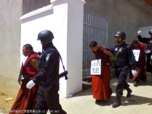 Reminiscent of the Cultural Revolution, at three least monks with placards around their necks are lead away from their monastery by armed security personnel.